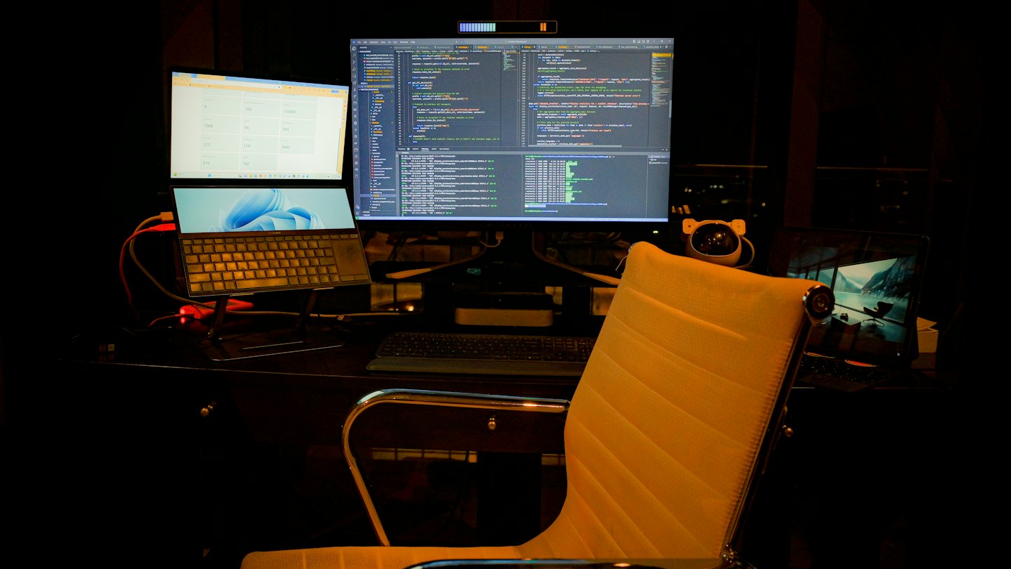 Multiple monitors displaying code on a desk with a yellow chair.